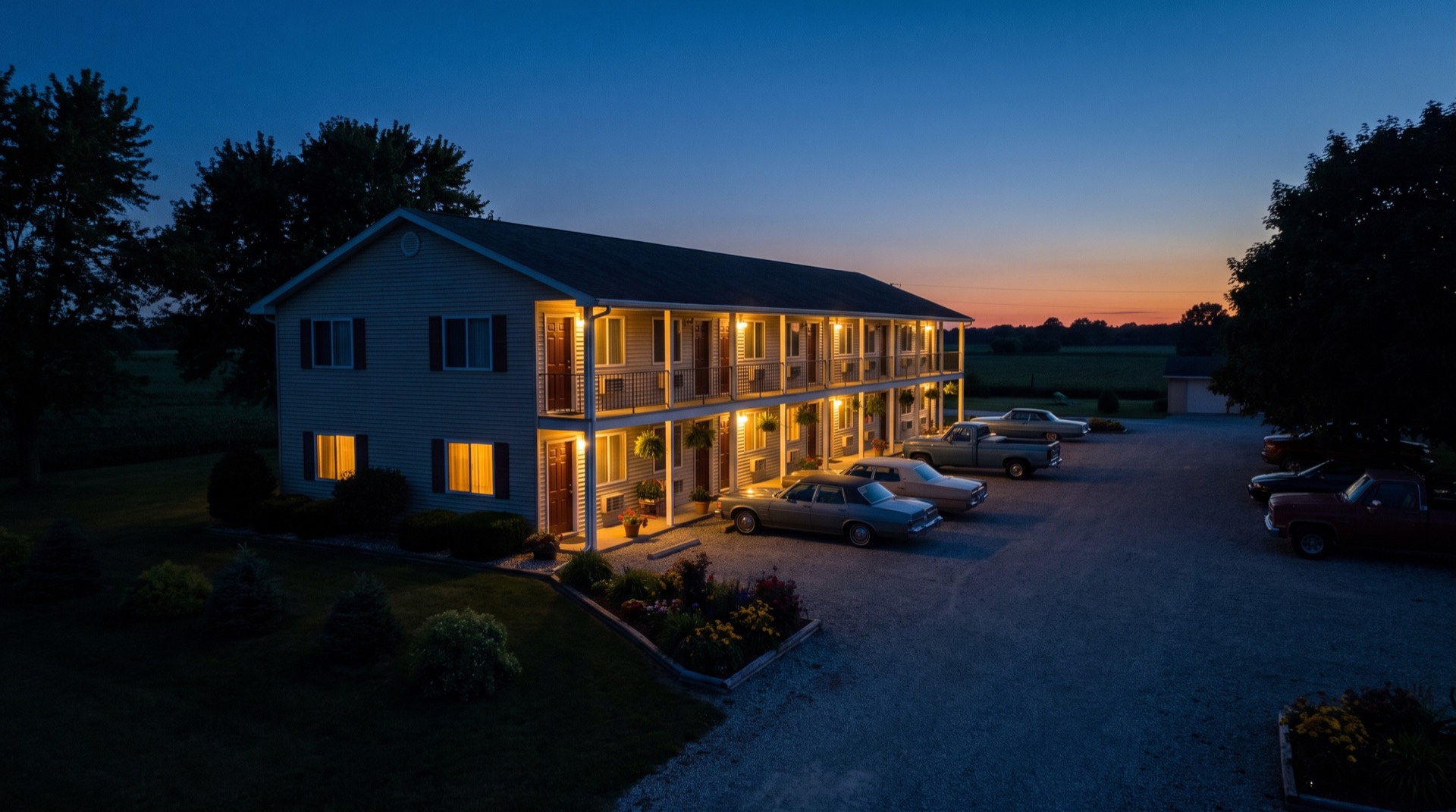 Illustrative image, not the actual property. A well kept two-story roadside motel at dusk with lit room windows and cars in the lot